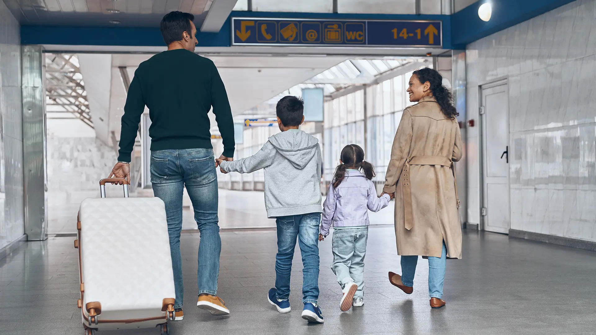 Full length rear view of family with two little kids walking by airport terminal