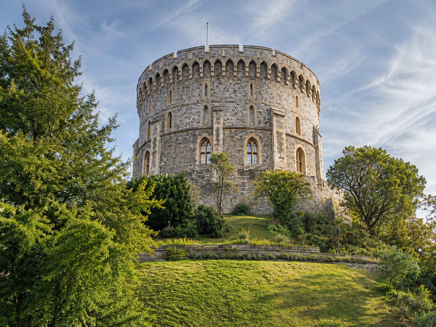 Windsor Castle Round Tower surrounded by landscaped gardens under a clear blue sky.